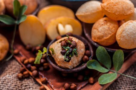 Famous Indian & Asian street food dish i.e. Panipuri snack in a clay bowl along with its flavored spicy water in another clay vessel. Entire consisting raw ingredients present on the surface.Top shot.の写真素材