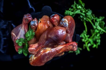 Raw cut unwashed chicken drumsticks in a steel plate isolated in black along with bunch of fresh parsley or coriander leaves on it. Vertical close up shot.の写真素材