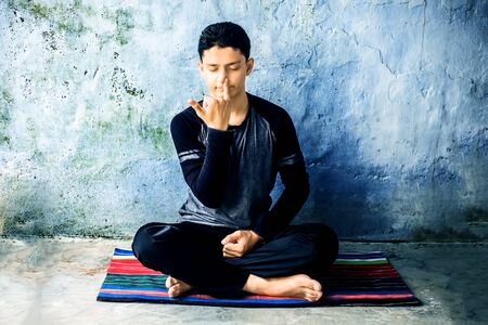 Portrait shot of the young man doing pranayama or pranayam or breath control yoga on a colorful mat with wearing black attire.の写真素材