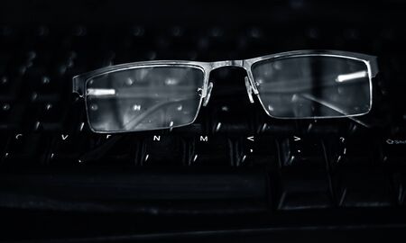 Black colored half-rim glasses or spectacles on a black colored desktop keyboard.の写真素材