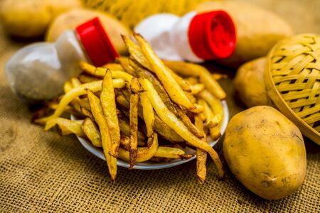 Fresh fired French fries of along with sprinkler of black pepper and salt on jute bag's surface and some raw potato also.の写真素材