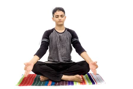 Portrait shot of the young man doing Lotus position or Padmasana or cross-legged sitting asana on a colorful mat with wearing black attire isolated on white background.の写真素材