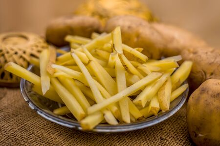 Raw cut french fries in a transparent glass plate along with raw potato with it on jute bag's surface.の写真素材