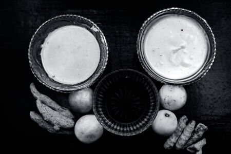 Face mask of lemon juice, honey, and curd along with some raw turmeric well mixed in a glass bowl along with entire raw ingredients on the wooden surface for acne-prone skin and blemishes.の写真素材