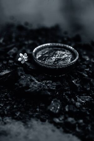 Close up of activated charcoal in a glass bowl on the wooden surface along with some raw powder of charcoal or coal spread on the surface.の写真素材
