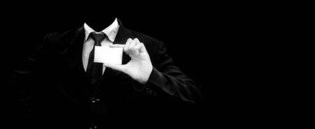 Unrecognizable faceless gentleman or seller holding white colored card in his hand wearing a dark blue colored suit with black necktie isolated on black.Concept of marketting.の写真素材