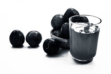 Raw organic red ripe plums in a brown-colored basket along with its extracted tincture or extracted water in a glass isolated on white.の写真素材