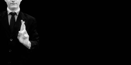 Businessman in a suit doing good luck sign with his hands isolated on a black colored background.の写真素材