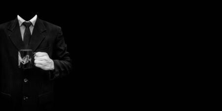 An unrecognizable office employee wearing a blue colored suit and posing with a cup of coffee in his hands isolated on a black colored background.の写真素材
