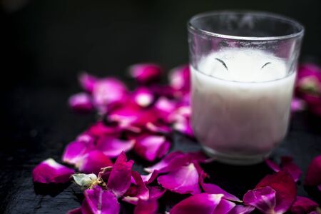 Fresh raw milk in a glass on a black surface along with some rose petals spread. Horizontal shot.の写真素材