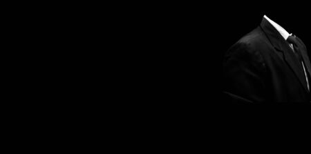 Faceless unrecognizable male wearing a blue colored suit with a black necktie and standing against a black background with good positive attitude. Wide-angle full resolution image.の写真素材