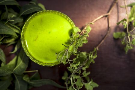 Close up shot of glass bowl full of tulsi or basil and neem or Indian lilac paste in it along with...