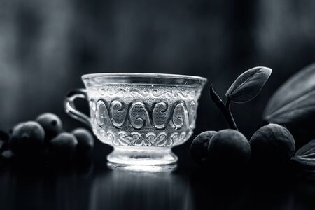 Detoxifying herbal ayurvedic banyan tree tea or Indian wishing tree tea in transparent glass cup along with some ripe and raw banyan fruit on a black glossy surface with blurred background.の写真素材