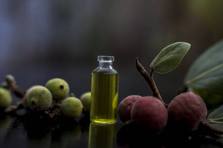 Close up shot of extracted herbal floral and beneficial Banyan tree essence in a tiny glass bottle on wooden surface along with its leaves and fruit.の写真素材