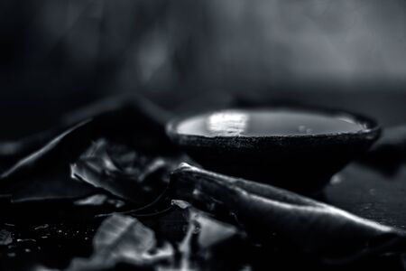 Close up shot of Banyan tree paste in a clay bowl on black glossy surface along with some dried leaf...