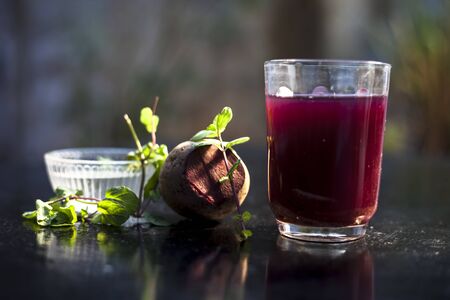 Beetroot smoothie in a glass on black glossy surface with some fresh mint leaves and water.Horizontal shot of beetroot smoothie along with some mint leaves. Shot with blurred background.の写真素材