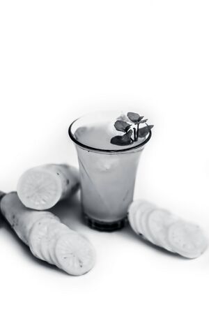 Close up shot of fresh daikon juice in a glass isolated on a white background along with some sliced daikon and some lemon. Vertical shot of daikon juice with some mint leaves on it.の写真素材