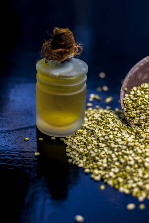 Close up of clay bowl full of a Green gram or mung bean or moong bean along with its extracted essential oil in a glass bottle beside it on a black surface. Vertical shot.の写真素材