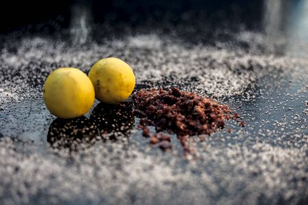 Pair of raw organic ripe yellow lemons on a black surface along with some rock salt (sendha namak) and white or common salt spread on the surface. Used for the salt remedy of skin and as a face mask.の写真素材