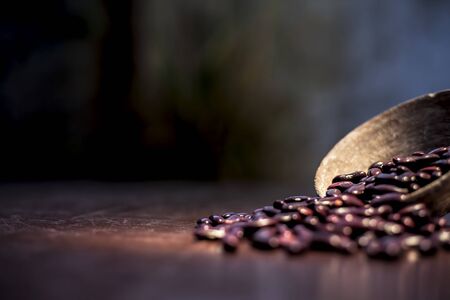Close up of raw kidney beans on brown colored surface in a clay bowl with a spotlight on it....