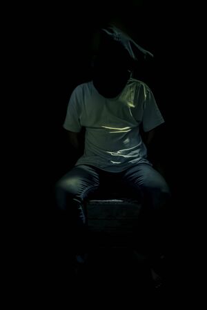 Adult human sitting on a rusted metal chair wearing a black colored bag covering his face.In dark gothic colors.の写真素材
