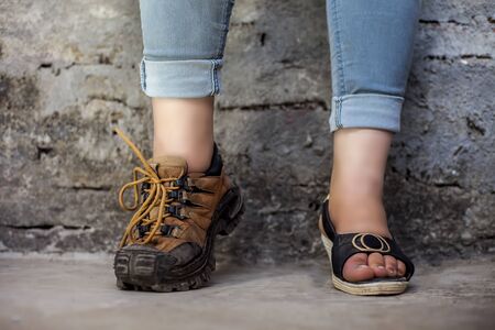 The elegant foot of young teenage girl wearing peep-toe sandals in one foot and hiking boots in...