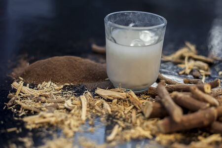 Licorice ayurvedic herb face mask for dark spots on a black wooden board consisting of some licorice powder, sandalwood powder, and milk. Shot of herb powder, raw herb, milk, and sandalwood powder.の写真素材