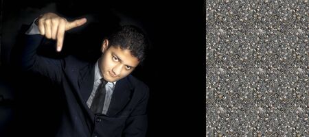 Portrait shot of an arrogant businessman posing on a black colored background in a blue suit with one hand pointing downwards showing arrogance on his face. Horizontal shot in high resolution.の写真素材