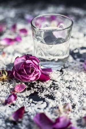 Close up shot of a glass of water along with some rose petals on a black board spread with some wheat flour. Concept of face mask applied in spa and cosmetic centre.の写真素材