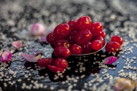 Close up of sweet cherries in a glass plate with some sugar and rose petals with it on a black colored wooden board.の写真素材