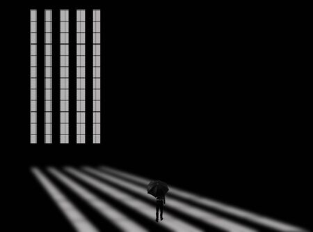 Creative shot of a long window with rays of light coming through it and falling on the floor along with a male walking with an umbrella in his hand. Horizontal shot in black and white colors.の写真素材