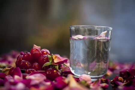 Face mask for naturally glowing skin on a black surface consisting of some sweet cherries well mixed with water. Shot of fresh cherries, a glass of water and some spread rose petals.の写真素材