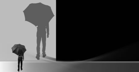 Creative minimalistic shot of a man standing holding a black umbrella and looking towards his enlarged magnified shadow on a creative wall. Horizontal shot in black and white colors.の写真素材