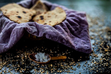 Close up shot of round bread Bhakri on the black wooden surface along with some raw whole wheat,...