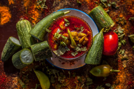 Close up shot of Gujarati famous Galka Nu Shaak on a glass plate. Shot of sponge gourd dish in a glass plate along with all the spices on a brown with some fresh tomatoes and sponge gourd.の写真素材