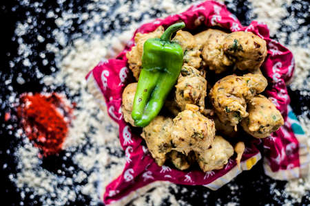 Famous Kanda bhaji or Kanda bhajiya or Kanda pakora in a container on a black surface along with...