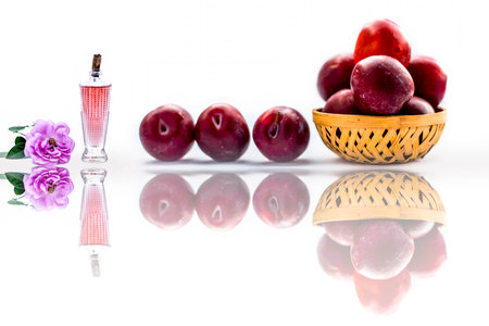 Raw organic red ripe plums in a brown-colored basket isolated on white along with some rose water in a bottle along with rose flowers used to make a face mask.の写真素材