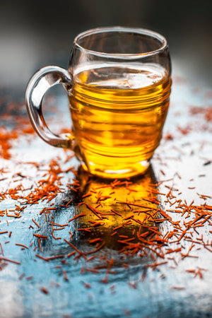 Saffron water in a big glass mug on a black-colored surface along with some saffron threads spread on the surface.の写真素材