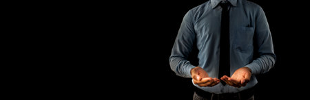A young male worker dressed in a blue shirt and black necktie with his hands holding something against black background isolated.の写真素材