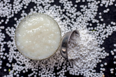 Close up shot of sabudana ki kheer in a glass bowl along with some raw tapioca pearls and sugar spread on the surface.の写真素材