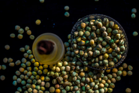 Shot of a bowl of green peas along with its extracted oil in a glass bottle on a black surface.の写真素材