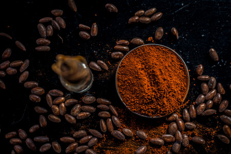 Coffee face mask for anti-aging on a black colored wooden surface consisting of some coffee beans and raw organic coconut oil in a small tiny glass bottle.の写真素材