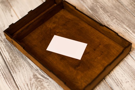 Dark wooden box with white card. Light wooden background. Space for text.の写真素材