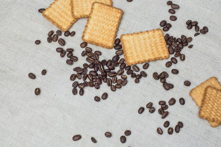 The background of a gray cloth made of old and coarse burlap, on which lies a certain amount of brown coffee beans with a yellow rectangular biscuitの写真素材