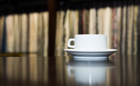 White ceramic cup and saucer on a dark wooden background. Place for your text. Reflection of the cup on the tableの写真素材