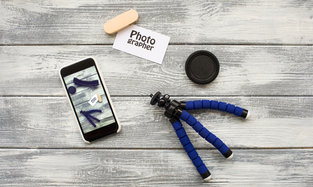 top view of workplace of photographer tripod, phone, flash drive and accessory for camera on wooden backgroundの写真素材
