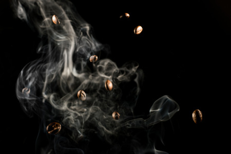 Coffee beans falling down trough smoke over black background - isolatedの写真素材
