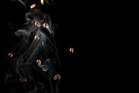 Coffee beans falling down trough smoke over black background - isolatedの写真素材