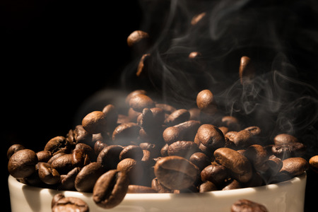 Coffee mug full of coffee beans with smokeの写真素材