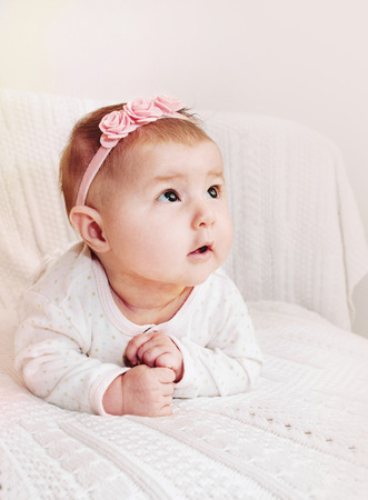cute little baby girl with pink flower headband exploring the world from the couchの写真素材